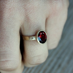 Puede incluir: Un anillo de oro con una piedra preciosa roja. El anillo est&aacute; en el dedo de una persona.