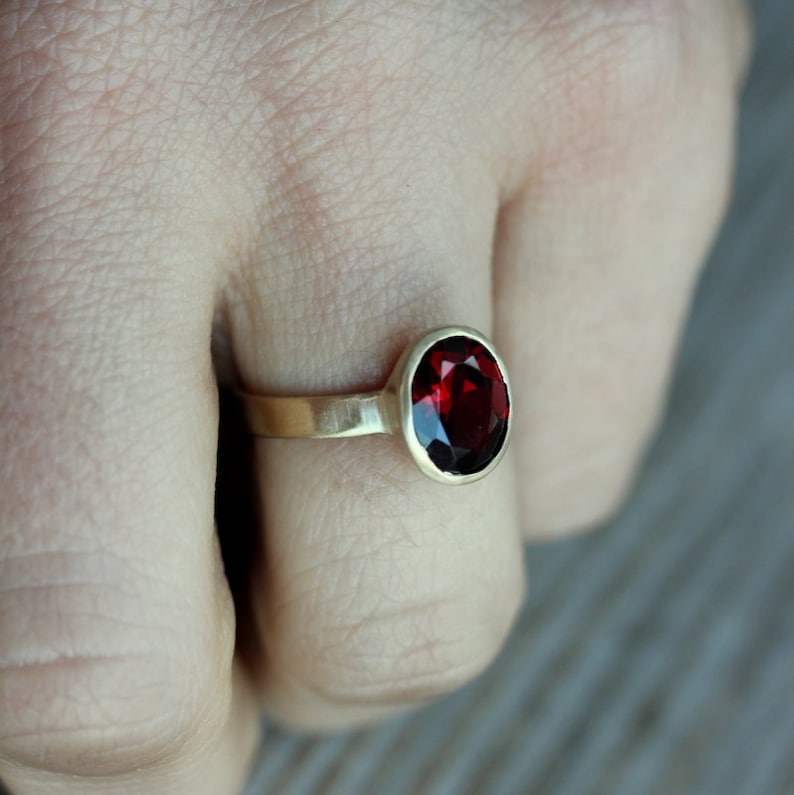Puede incluir: Un anillo de oro con una piedra preciosa roja. El anillo est&aacute; en el dedo de una persona.