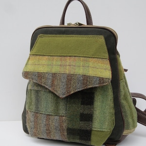 May include: A backpack featuring a patchwork design of green, brown, and grey wool-like fabrics. The bag includes a top handle, a front flap pocket with a pointed edge, and dark brown leather-like straps. The exterior displays various textures.