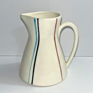 Peut inclure: Pichet en céramique crème avec une anse et un bec verseur incurvés. Des rayures verticales noires, bleues et rouges ornent le devant. Le pichet a une base légèrement évasée et une finition lisse et brillante. Une pièce décorative de style vintage.