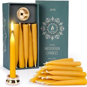 May include: A set of 20 yellow beeswax meditation candles in a dark green box with a gold-colored metal candle holder. One candle is lit and standing in the holder. The box features a mandala design and the text AGLARY BEESWAX MEDITATION CANDLES.
