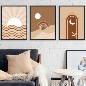 Op de afbeelding: Drie abstracte kunstprints met een minimalistisch ontwerp. De prints tonen een zon, een halve maan en een geometrische boog. De prints zijn in tinten bruin, beige en wit.