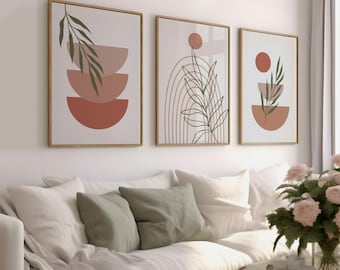 May include: Three framed abstract art prints with botanical and geometric designs. The prints feature earth-tone colors, including terracotta, beige, and olive green. The artwork is displayed above a white sofa with green pillows.