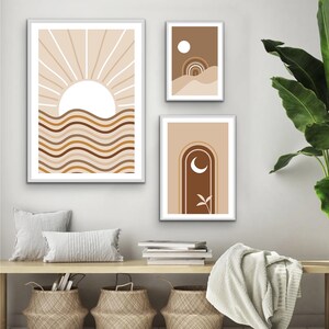 Op de afbeelding: Drie abstracte kunstprints met een minimalistisch ontwerp met een zon, maan en boog in tinten bruin, beige en wit.