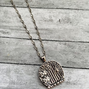 May include: A silver necklace with a detailed charm of a small door with a knocker. The door is surrounded by a decorative frame.