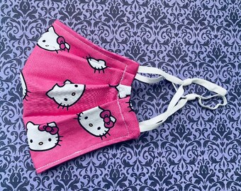 May include: Pink face mask with a white Hello Kitty print. The mask has white elastic straps.