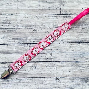May include: Pink and white baby pacifier clip with a silver clip and a repeating pattern of cartoon cats.