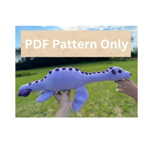 May include: A crocheted purple dinosaur with a long neck and a textured surface. The dinosaur has purple spots and black eyes. The text "PDF Pattern Only" is visible in the image.