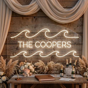 Puede incluir: Un letrero de acrílico transparente con tubos de neón blanco cálido que forman patrones de olas sobre y debajo del texto THE COOPERS. El letrero está montado en una pared de madera rústica con tela drapeada sobre una mesa con flores.
