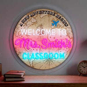 Op de afbeelding: Een ronde, verlichte bewegwijzering met een wereldkaartontwerp. Het bord toont de tekst "A NEW ADVENTURE BEGINS" en "WELCOME TO Mrs. Smith's CLASSROOM" in neonlicht. Een kleine vliegtuigafbeelding is ook inbegrepen.