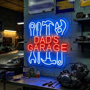 May include: A neon sign that reads "DAD'S GARAGE" in red and blue. The sign features tool outlines and is mounted on a brick wall. The garage setting includes tools, car parts, and a vintage car.