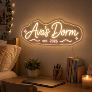 May include: A wall-mounted neon sign with a warm white glow, featuring the cursive text "Ava's Dorm" and "est. 2026" inside a cloud-shaped outline. The sign includes two small star icons and two wavy lines, all illuminated against a neutral wall.