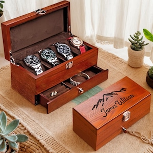 May include: A wooden watch box with a drawer, featuring a personalized inscription "James Wilson" and a mountain design. The box has a hinged lid and a pull-out drawer for storing watches and other accessories.