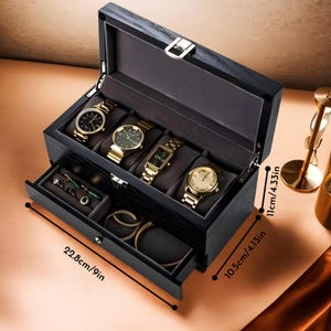 May include: Black wooden watch box with a drawer. The box has five slots for watches and measures 9 inches by 4.13 inches by 4.33 inches.