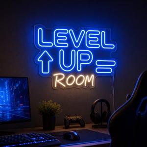 May include: A wall-mounted neon sign featuring the text LEVEL UP in bright blue, an upward arrow, an equals sign, and the word ROOM in warm white. The sign has a contoured backing and is illuminated against a dark wall above a gaming desk setup.