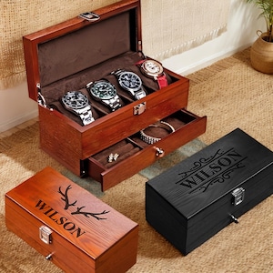 May include: Two wooden watch boxes with a drawer. The top box is brown with a black interior and has five slots for watches. The bottom box is black with a wood grain pattern and has a hinged lid. Both boxes have the name "WILSON" engraved on the front.