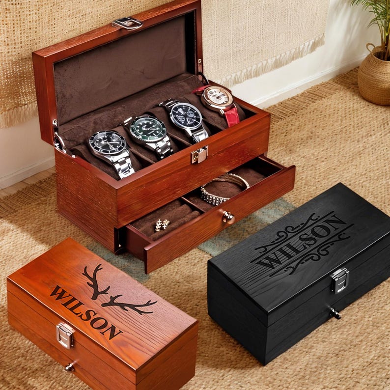 May include: Two wooden watch boxes with a drawer. The top box is brown with a black interior and has five slots for watches. The bottom box is black with a wood grain pattern and has a hinged lid. Both boxes have the name "WILSON" engraved on the front.