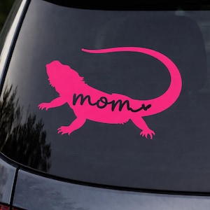 May include: A pink bearded dragon decal with the word "mom" in cursive. The sticker is applied to a car window, featuring a pet-themed design, suitable for reptile enthusiasts.