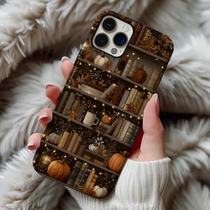 May include: A smartphone case featuring a printed design of wooden bookshelves filled with various books, small pumpkins, and glowing string lights. The color palette includes shades of brown, orange, cream, and dark tones, creating a detailed autumn-themed scene across the entire back surface of the protective cover.