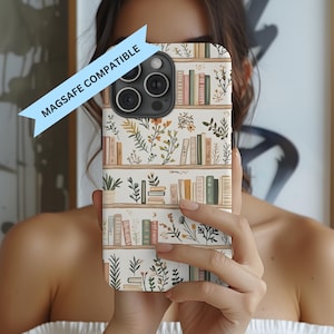 May include: A white phone case with a bookshelf design. The case features rows of books in various colors, interspersed with floral and plant illustrations. The text "MAGSAFE COMPATIBLE" is displayed on a blue banner.