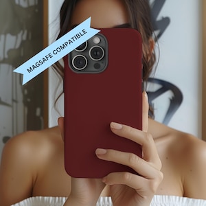 May include: A burgundy phone case with a camera lens cutout and the text "MAGSAFE COMPATIBLE" on a blue ribbon.