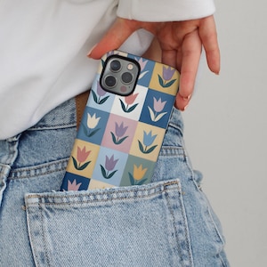 May include: A colorful phone case featuring a tulip pattern in a grid design. The case has a square pattern with tulips in various colors, including pink, yellow, and purple, set against a light blue, yellow, and green background. The phone case is in a denim pocket.