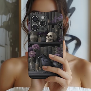 May include: A phone case featuring a gothic design with a bookshelf, skull, raven, and purple flowers. The case has a dark color scheme with detailed illustrations of books, bottles, and a raven. The design evokes a mysterious and vintage aesthetic.