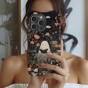 May include: Black phone case featuring a whimsical illustration of a ghost reading a book amidst flowers and stacked books. The case has a dark background with floral and cloud accents, and a brick-like border.