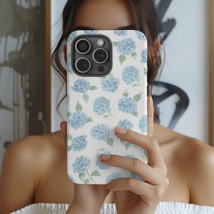 May include: A white phone case with a blue floral pattern. The case has a camera lens cutout and a white background.