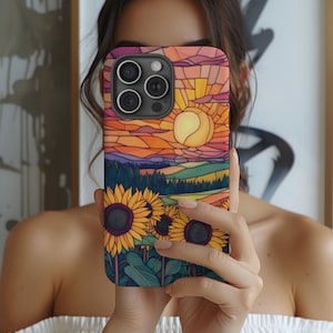 May include: A colorful phone case with a stained glass design featuring a sunset, a field of sunflowers, and a sun. The case is made for an iPhone with a camera bump.