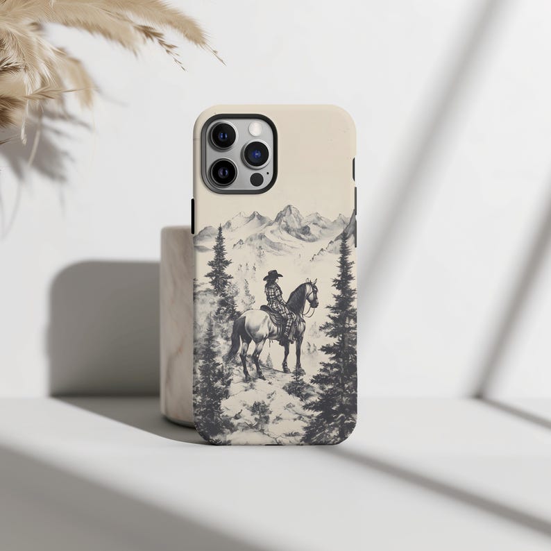 May include: A white iPhone case featuring a black and white illustration of a person riding a horse in a mountainous scene.