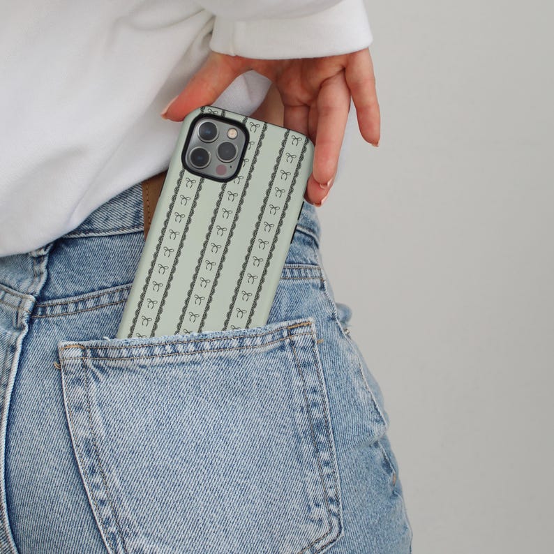 Pode incluir: Uma capa de telefone verde claro com um padr&atilde;o repetido de 3 pretos e um la&ccedil;o preto. A capa est&aacute; no bolso de tr&aacute;s de uma cal&ccedil;a jeans azul.