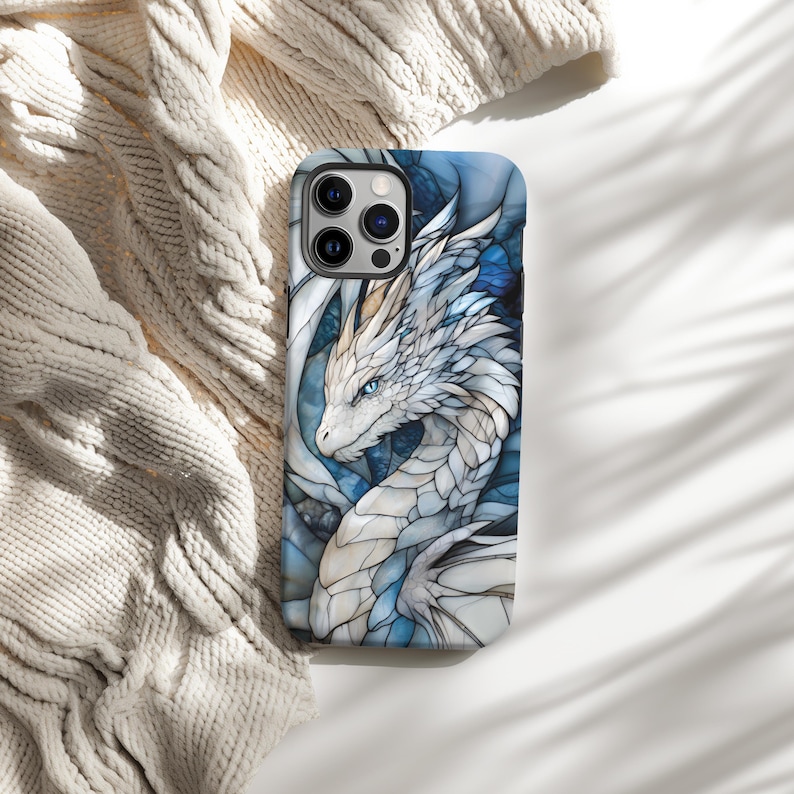 May include: A white and blue stained glass phone case featuring a dragon design. The dragon has blue eyes and is facing left. The phone case is for an iPhone 14 Pro.
