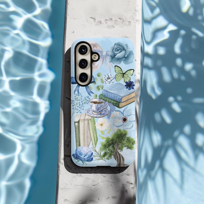 May include: A blue phone case with a watercolor design featuring flowers, books, a butterfly, and a teacup. The case has a camera cutout and a white background.