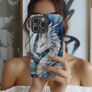 May include: A white and blue phone case featuring a dragon design. The dragon is white with blue accents and has a blue eye. The phone case is made from a hard plastic material.