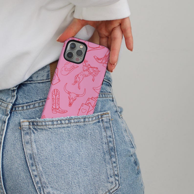 May include: A pink phone case with a red line drawing pattern of cowboy boots, hats, and other western-themed imagery.