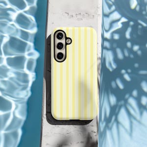 Pode incluir: Uma capa de telefone listrada amarela e branca com uma lente de c&acirc;mera preta.