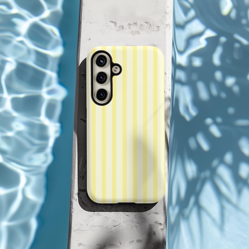 Pode incluir: Uma capa de telefone listrada amarela e branca com uma lente de c&acirc;mera preta.
