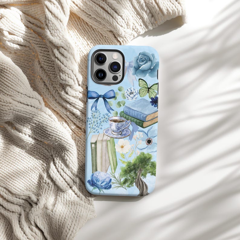 May include: A blue phone case with a watercolor design featuring books, flowers, a butterfly, a teacup, and a tree. The case has a camera cutout and a blue background.