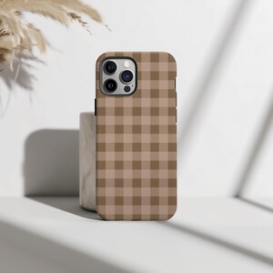 May include: A brown and tan plaid phone case. The case has a grid pattern of alternating light and dark brown squares. The phone case has a camera and flash opening on the top left corner.