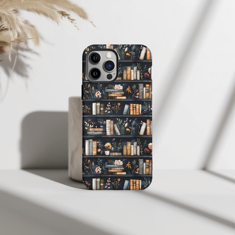 Pu&ograve; includere: Una custodia per telefono nera con un motivo di librerie piene di libri e fiori. La custodia ha un ritaglio per la fotocamera e uno sfondo nero.