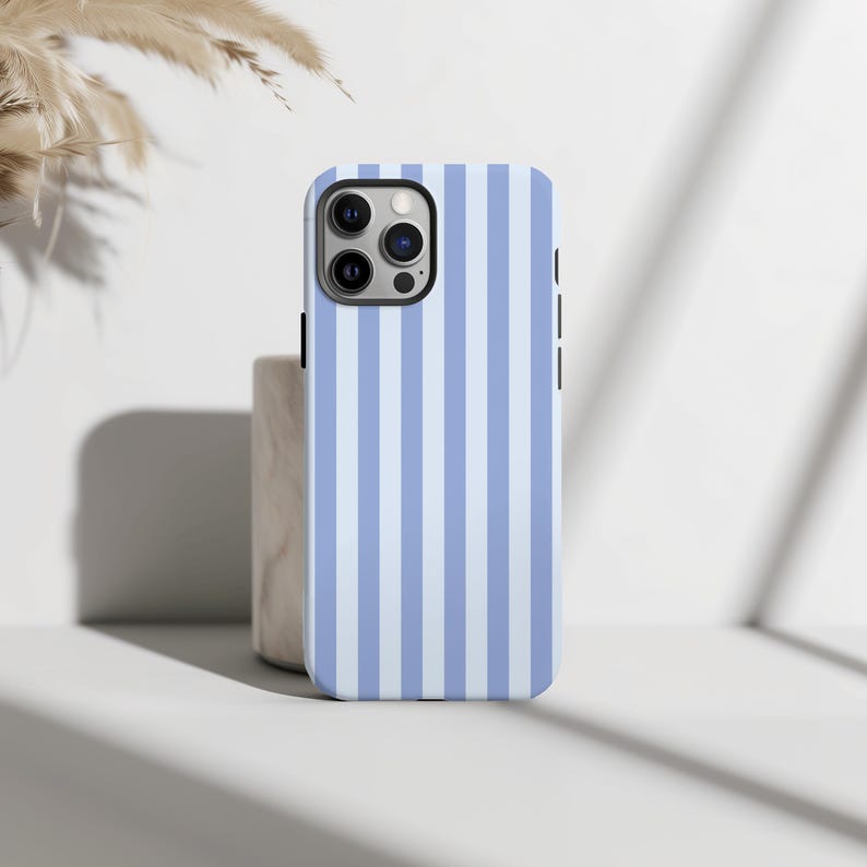 Peut inclure: Coque de smartphone &agrave; rayures verticales bleues claires et blanches. La coque a une finition brillante et une d&eacute;coupe pour l'appareil photo en haut &agrave; gauche. Pos&eacute;e sur une surface blanche.