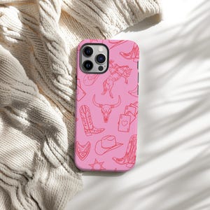 May include: Pink phone case with a red line drawing pattern of cowboy boots, a cowboy hat, a skull, a bull, and playing cards.