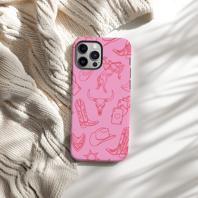 May include: Pink phone case with a red line drawing pattern of cowboy boots, a cowboy hat, a skull, a bull, and playing cards.
