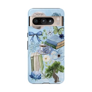 May include: A blue phone case with a watercolor design featuring books, flowers, a butterfly, a cup of tea, and a moon. The case has a cutout for the camera lens.