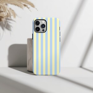 Op de afbeelding: Een smartphonehoesje met een verticaal streepjespatroon in afwisselend lichtblauw en geel. De hoes heeft een zwarte rand en een camera-uitsparing. De hoes ligt op een wit oppervlak.