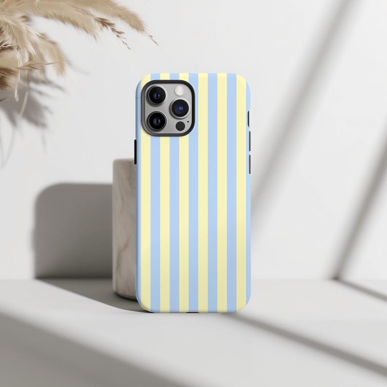Op de afbeelding: Een smartphonehoesje met een verticaal streepjespatroon in afwisselend lichtblauw en geel. De hoes heeft een zwarte rand en een camera-uitsparing. De hoes ligt op een wit oppervlak.