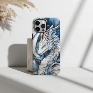 May include: A white and blue phone case featuring a dragon design. The dragon is white with blue accents and has a detailed, stained glass appearance.