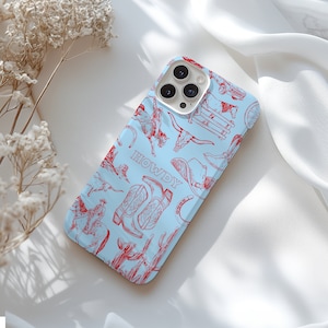 K&ouml;nnte beinhalten: Eine hellblaue iPhone-H&uuml;lle mit einem rot-wei&szlig;en Western-Design. Die H&uuml;lle zeigt verschiedene Bilder, darunter Cowboystiefel, Hufeisen und einen Cowboyhut. Der Text "HOWDY" ist auf der H&uuml;lle aufgedruckt.