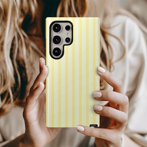 Pode incluir: Uma capa de telefone listrada amarela e branca com um recorte de c&acirc;mera preto.